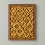 A square framed wall art piece featuring a mustard yellow macrame rope pattern in an openwork design, set in a medium brown wood frame against a light gray background.