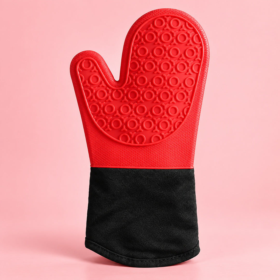 A silicone oven mitt with a textured red top half and a black fabric cuff, standing upright on a solid pink background.