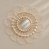 A circular wall mirror with a natural rattan or wicker frame arranged in a sunflower-like pattern, mounted on a neutral beige wall.