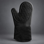 A single black oven mitt with a textured, circular-patterned non-slip grip and a solid black fabric cuff, photographed against a dark gray studio background.