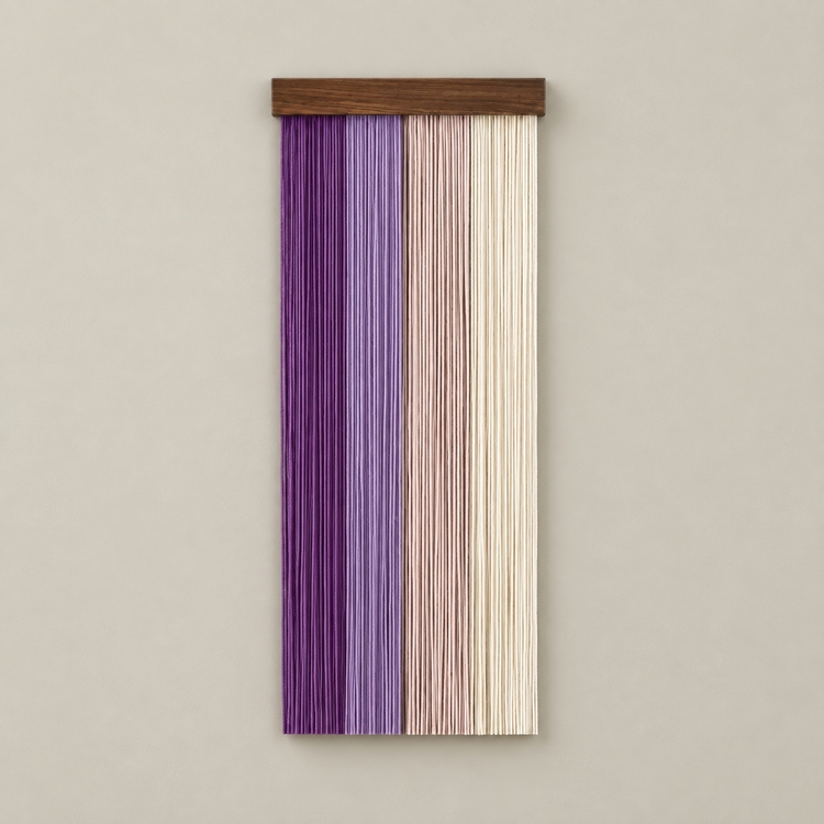 A vertical wall hanging made of narrow vertical slats in three color bands: purple, lavender, and cream, suspended from a dark wood bar against a plain beige wall.