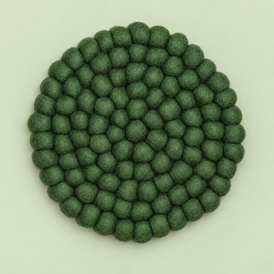 A round felt mat made of small textured pom-pom balls in a muted sage green color, photographed from directly above on a light off-white background.