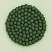 A round felt mat made of small textured pom-pom balls in a muted sage green color, photographed from directly above on a light off-white background.