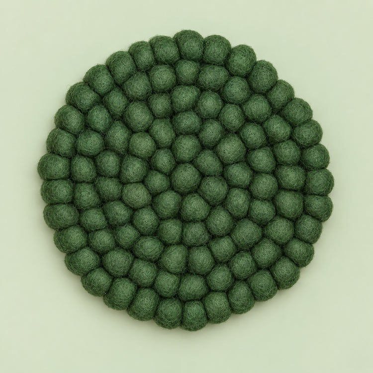 A round felt mat made of small textured pom-pom balls in a muted sage green color, photographed from directly above on a light off-white background.