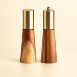 Set variant: one acacia wood salt shaker and one pepper grinder on a pale golden studio background.