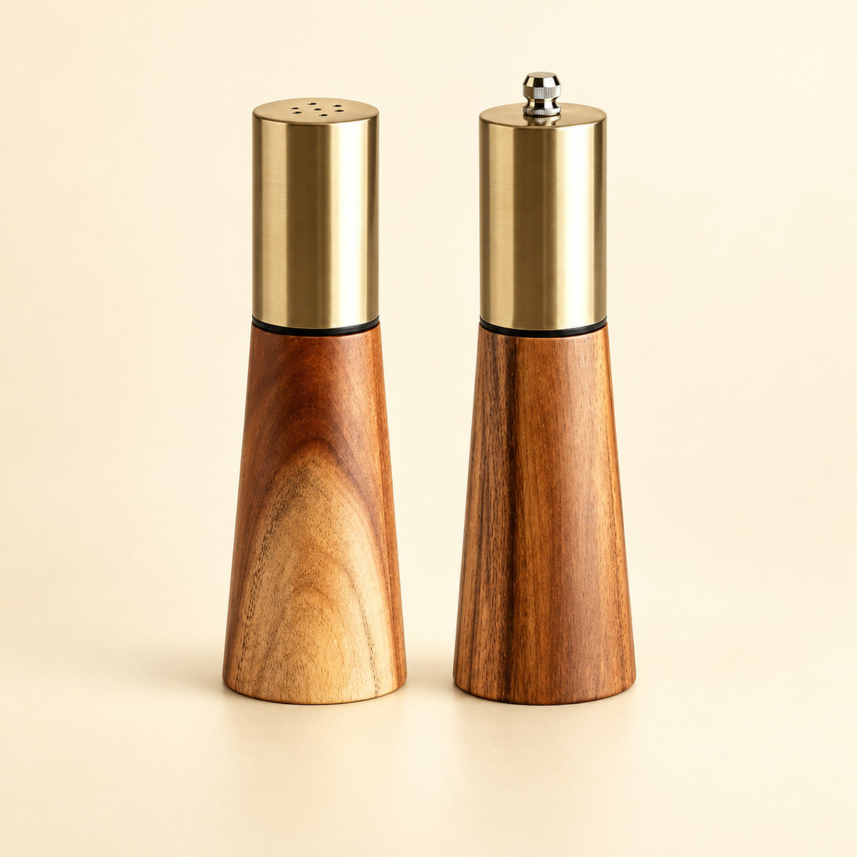 Set variant: one acacia wood salt shaker and one pepper grinder on a pale golden studio background.