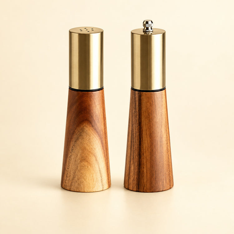 Set variant: one acacia wood salt shaker and one pepper grinder on a pale golden studio background.