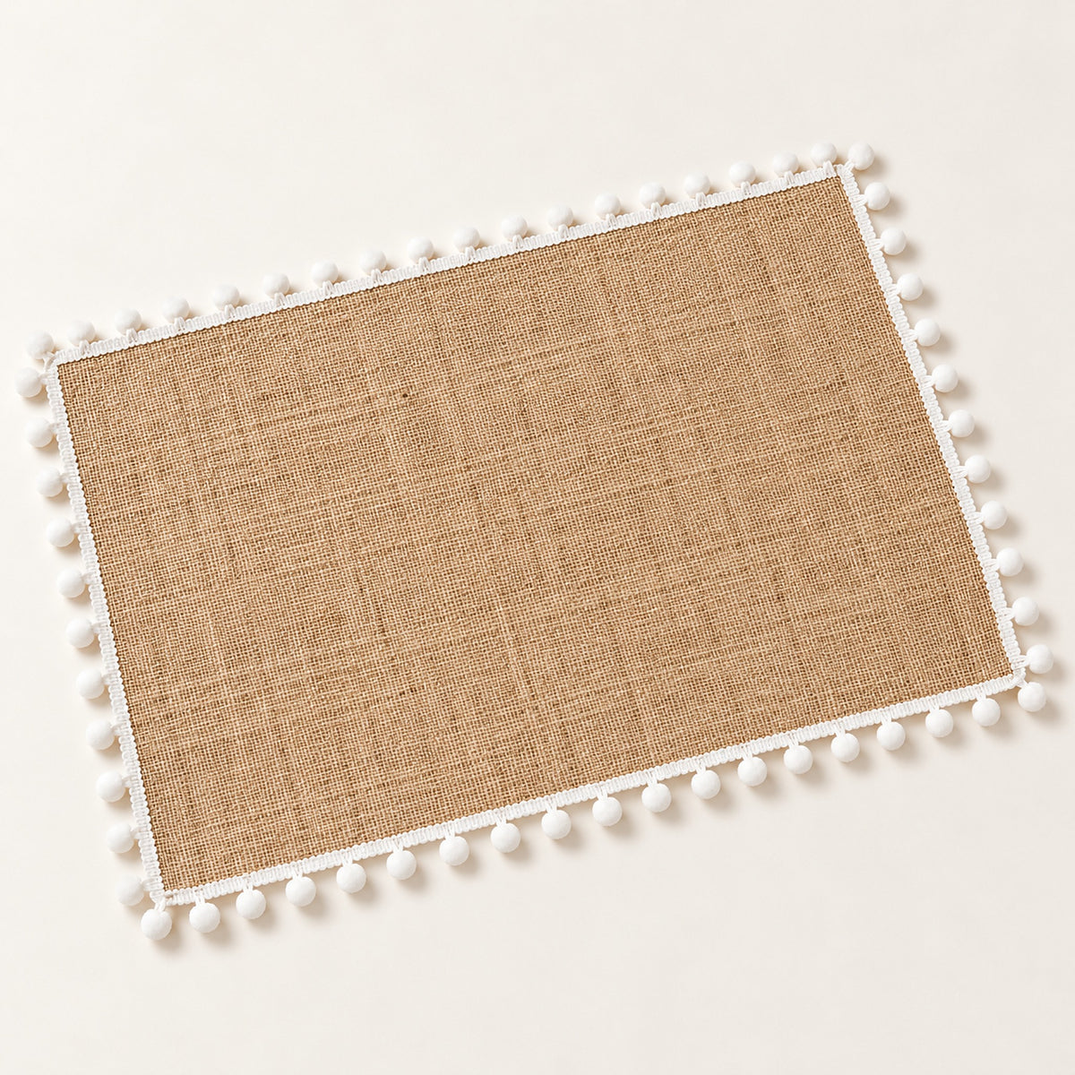 One tan placemat with white pom pom trim, 30 x 45 cm.