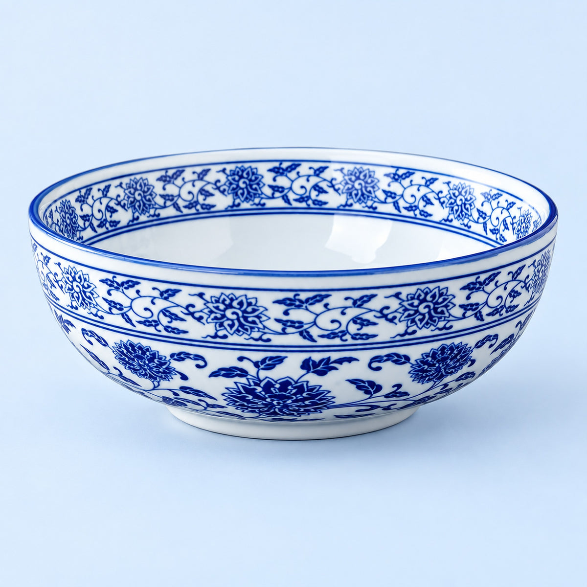 A white ceramic bowl decorated with traditional blue floral and vine patterns, shown against a light blue background.