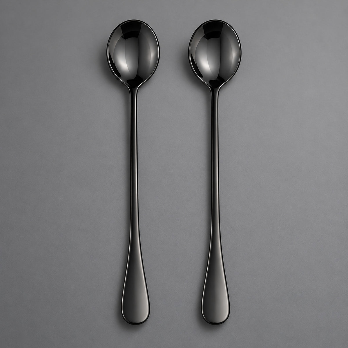 Two slim black metal spoons with a glossy finish, arranged vertically side-by-side on a neutral gray background.