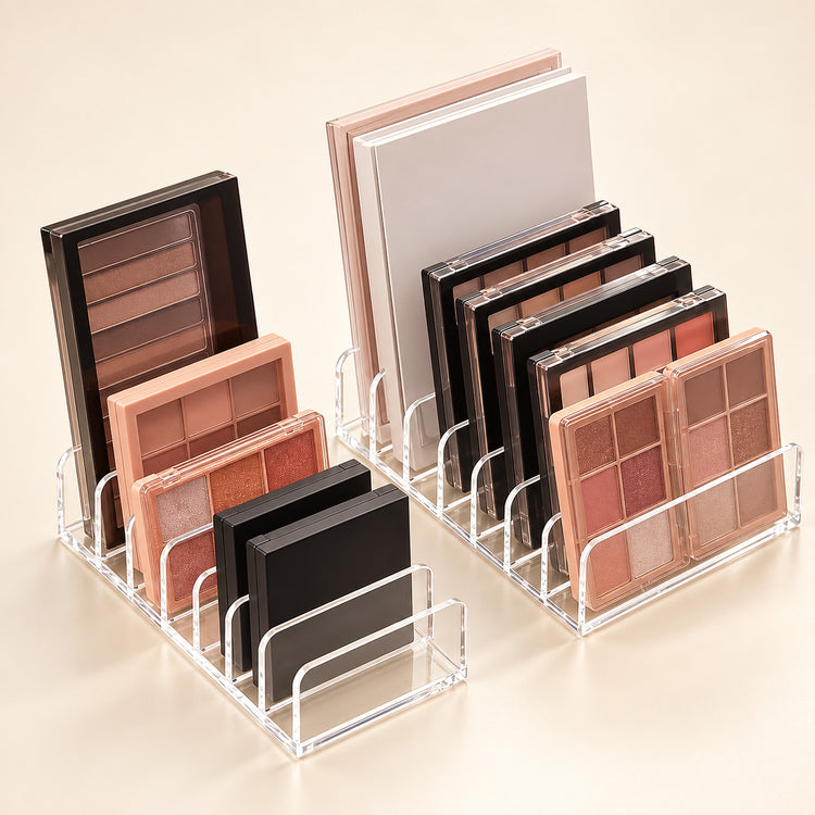 Two clear acrylic makeup organizer stands holding multiple eyeshadow palettes and compact powders in neutral and pink tones, arranged on a warm beige studio background.