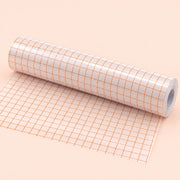 A roll of white adhesive tape with an orange grid pattern, partially unrolled on a solid pale peach background.