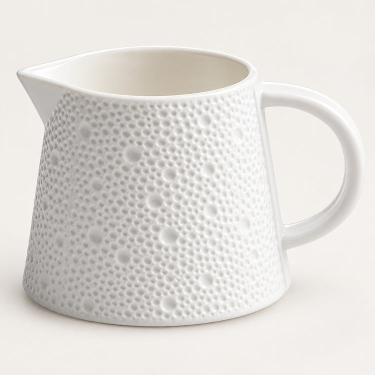 A white ceramic pitcher with a textured, dimpled surface pattern and a curved handle, shown on a light cream background.