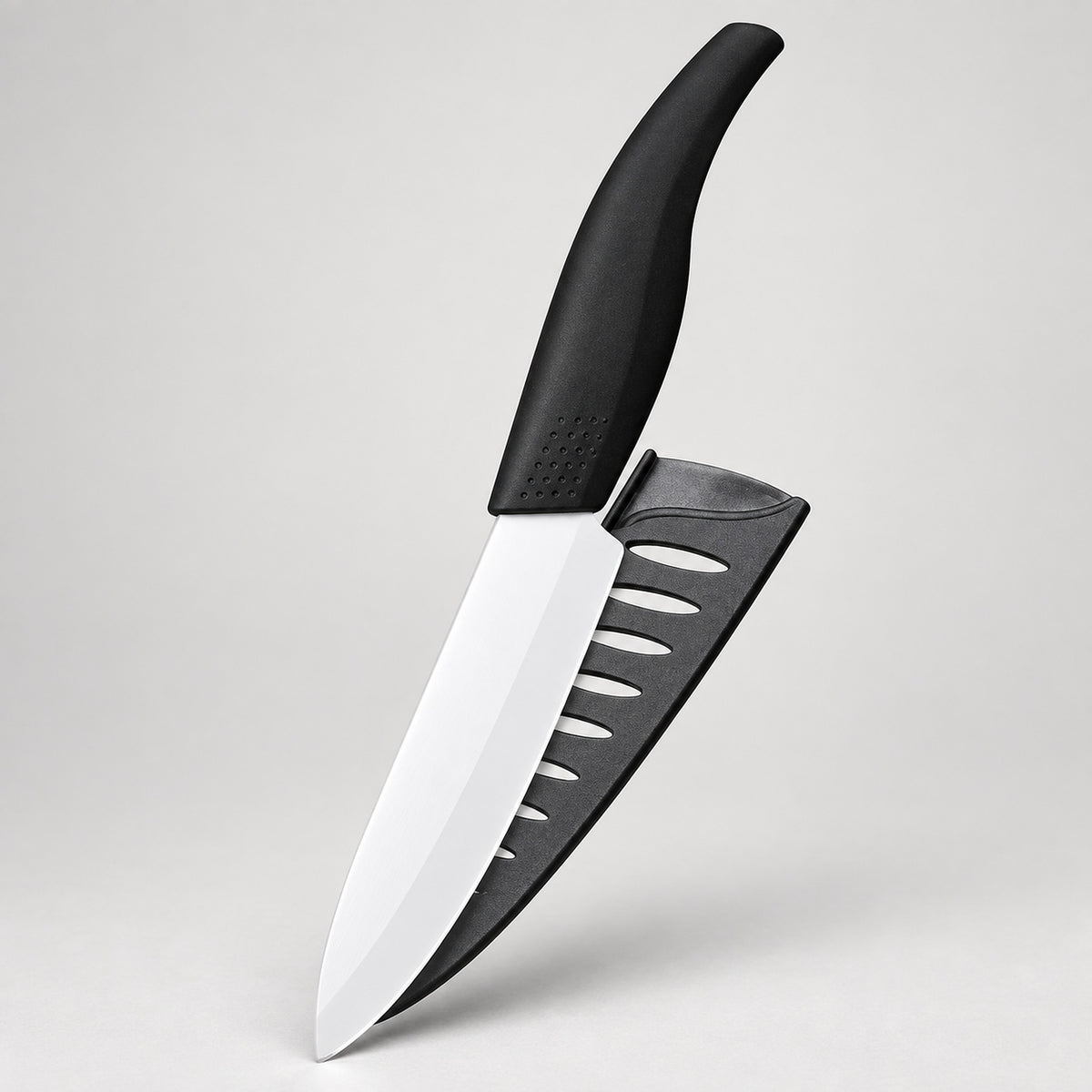 A kitchen knife with a black handle and a black sheath featuring diagonal cutouts, displayed against a neutral light gray background.