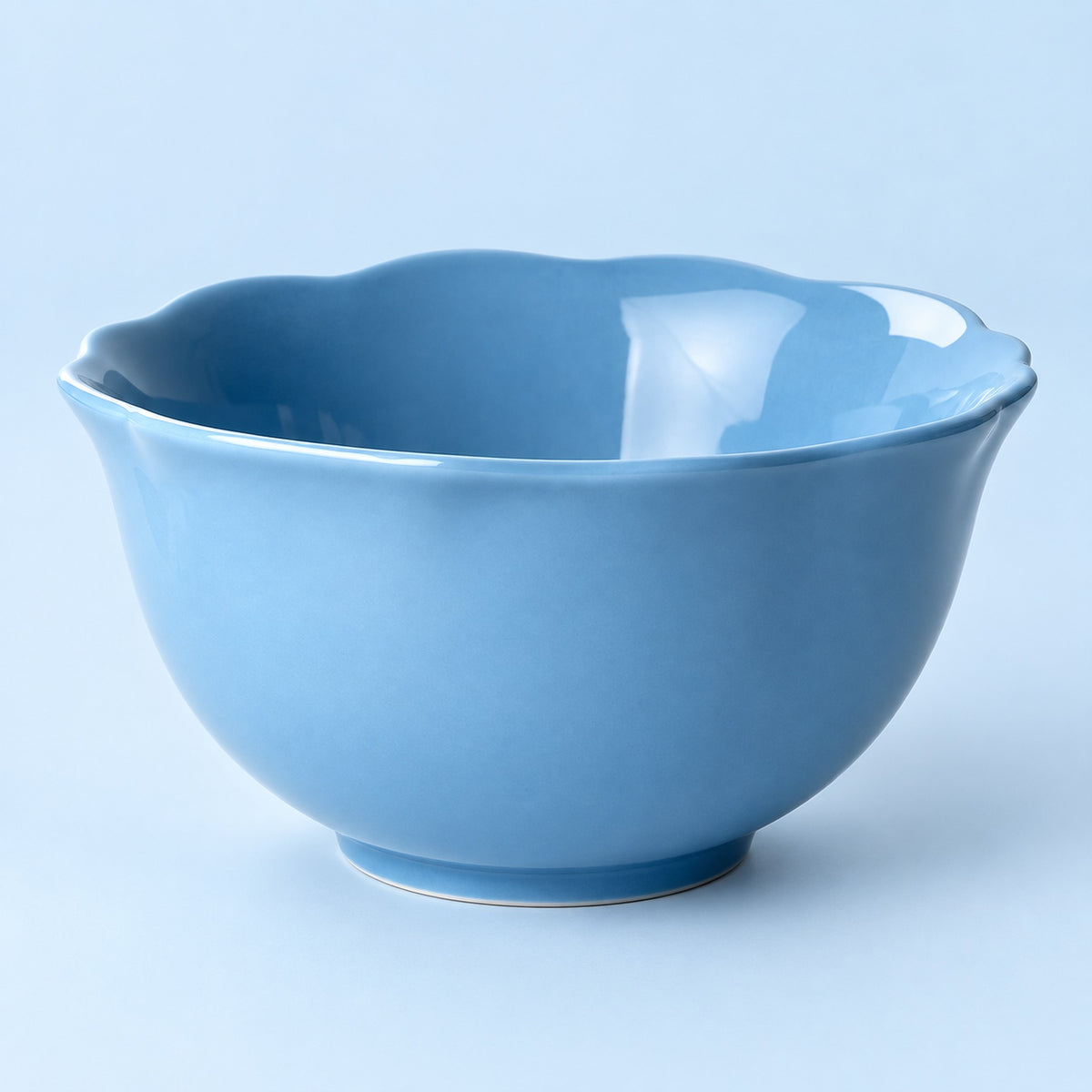A light blue ceramic bowl with a scalloped rim, photographed against a solid light blue background.