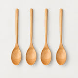Four Camel wood spoons on a light warm-gray studio background.