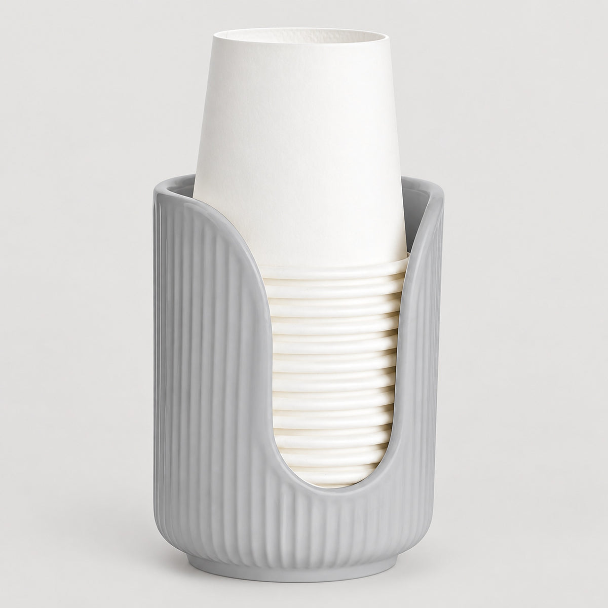 A light gray ribbed cup holder or cup dispenser holding a stack of white paper cups, photographed on a clean light gray background.