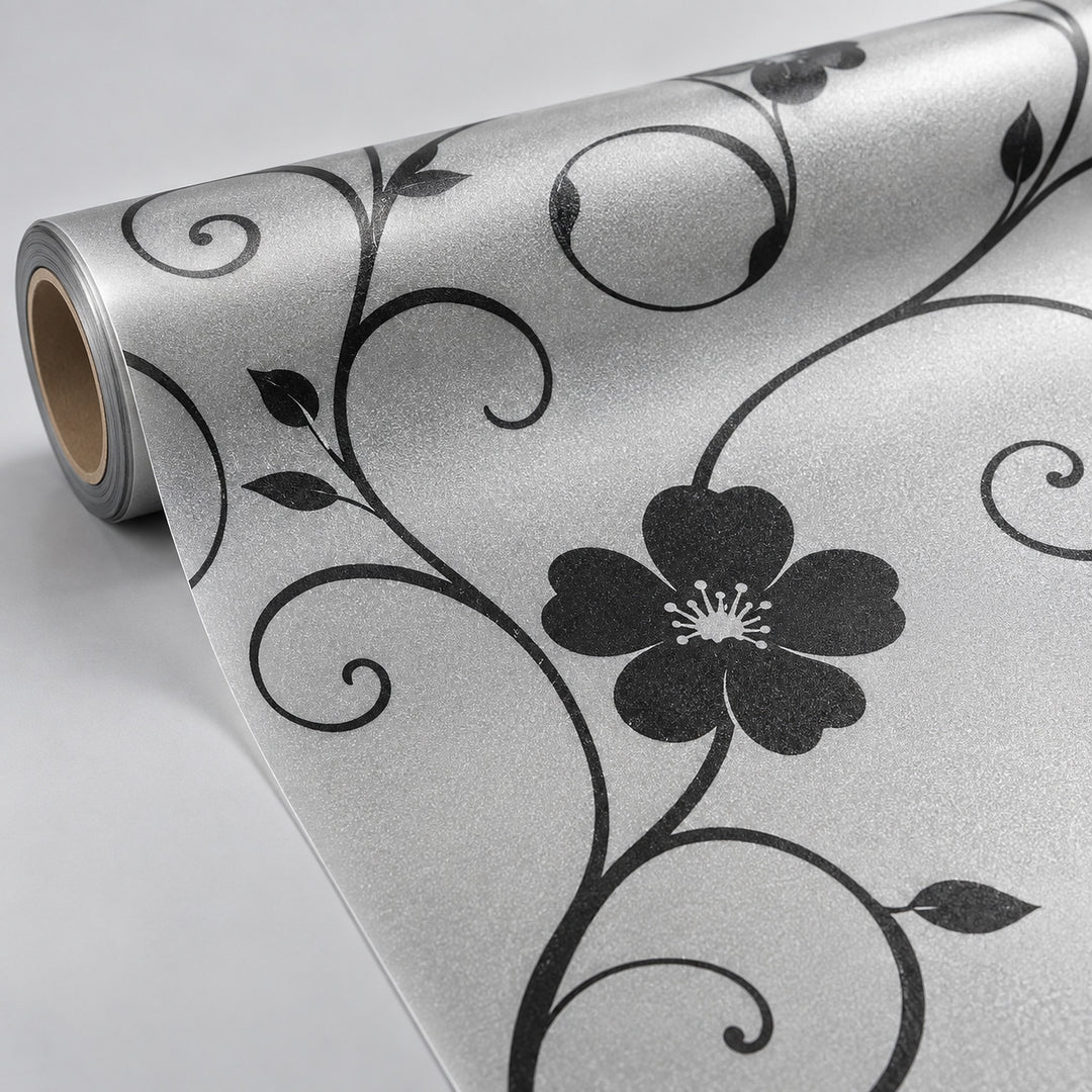 A roll of shimmering silver wrapping paper with a black floral vine pattern, partially unrolled to show the design and texture.