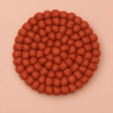 A round felt wall hanging or decorative plaque made of many small textured pom-pom balls, shown from above on a solid peach background.