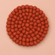 A round felt wall hanging or decorative plaque made of many small textured pom-pom balls, shown from above on a solid peach background.