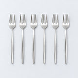 Set of six silver dinner forks on a pale gray studio background.