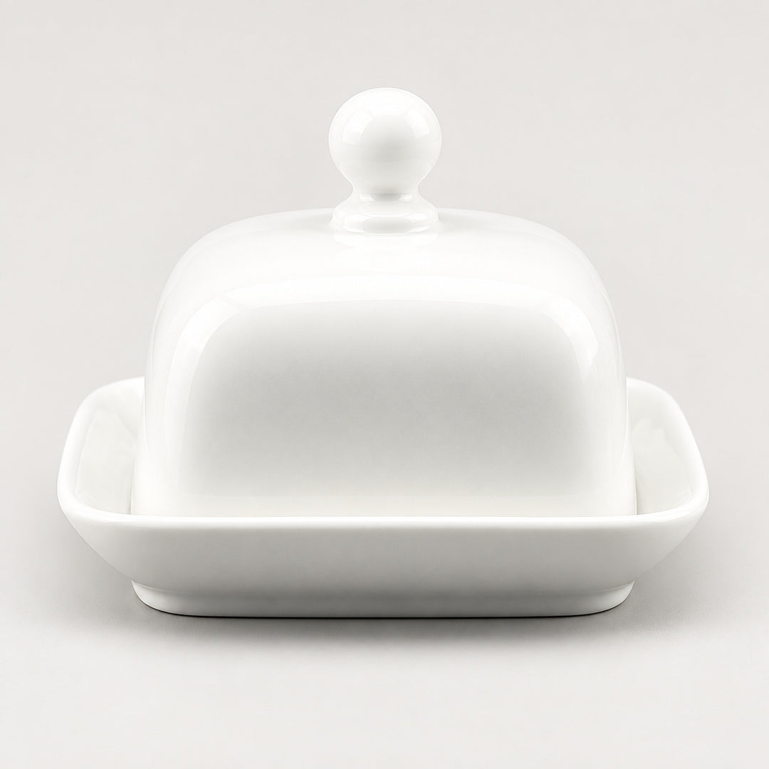 A white ceramic butter dish with a domed lid featuring a round knob and a shallow square base, photographed on a clean light gray background.