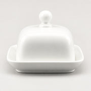 A white ceramic butter dish with a domed lid featuring a round knob and a shallow square base, photographed on a clean light gray background.