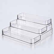 Three clear acrylic tiered storage trays stacked on a light gray reflective surface.