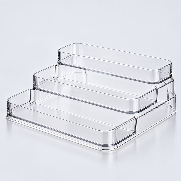 Three clear acrylic tiered storage trays stacked on a light gray reflective surface.