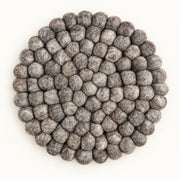 A round gray felt placemat made of textured, raised pom-pom balls, photographed from directly above on a clean white background.