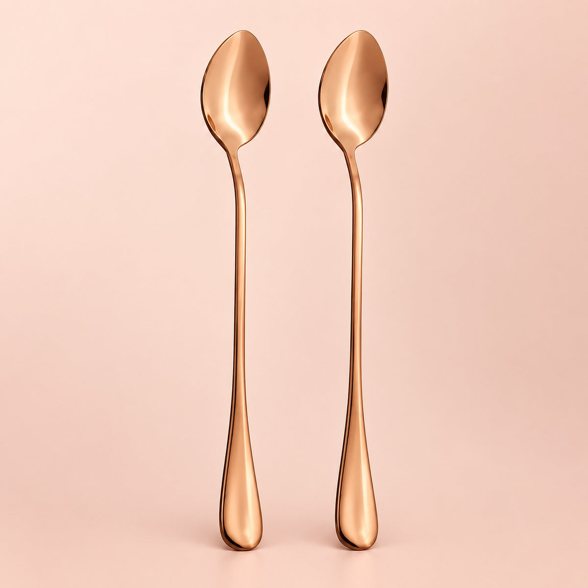 Two long-handled spoons with a polished rose gold metallic finish, standing upright side-by-side against a solid pale pink background.