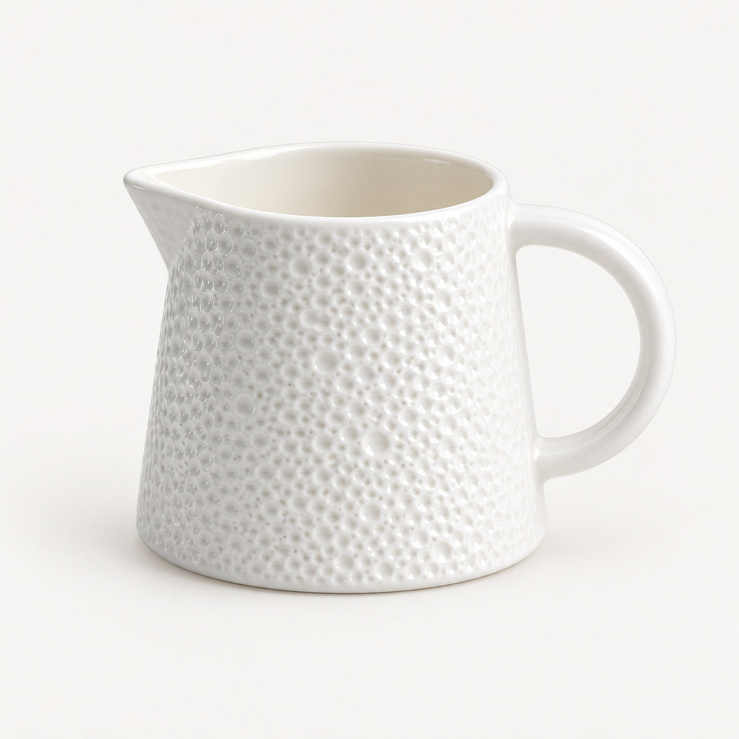 A white ceramic pitcher with a textured, dimpled surface pattern and a curved handle, shown on a clean white background.