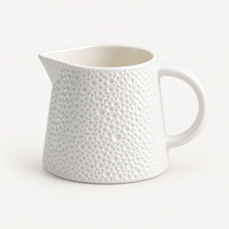 A white ceramic pitcher with a textured, dimpled surface pattern and a curved handle, shown on a clean white background.