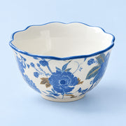 A ceramic bowl with a scalloped rim, featuring a blue and gold floral pattern on a white background, set against a light blue backdrop.