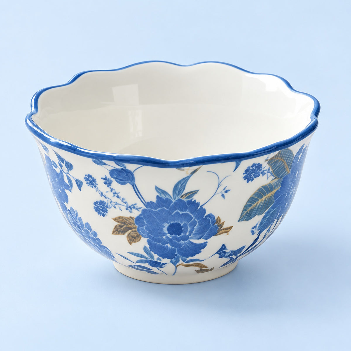 A ceramic bowl with a scalloped rim, featuring a blue and gold floral pattern on a white background, set against a light blue backdrop.