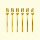 Set of six gold dinner forks on a pale yellow studio background.