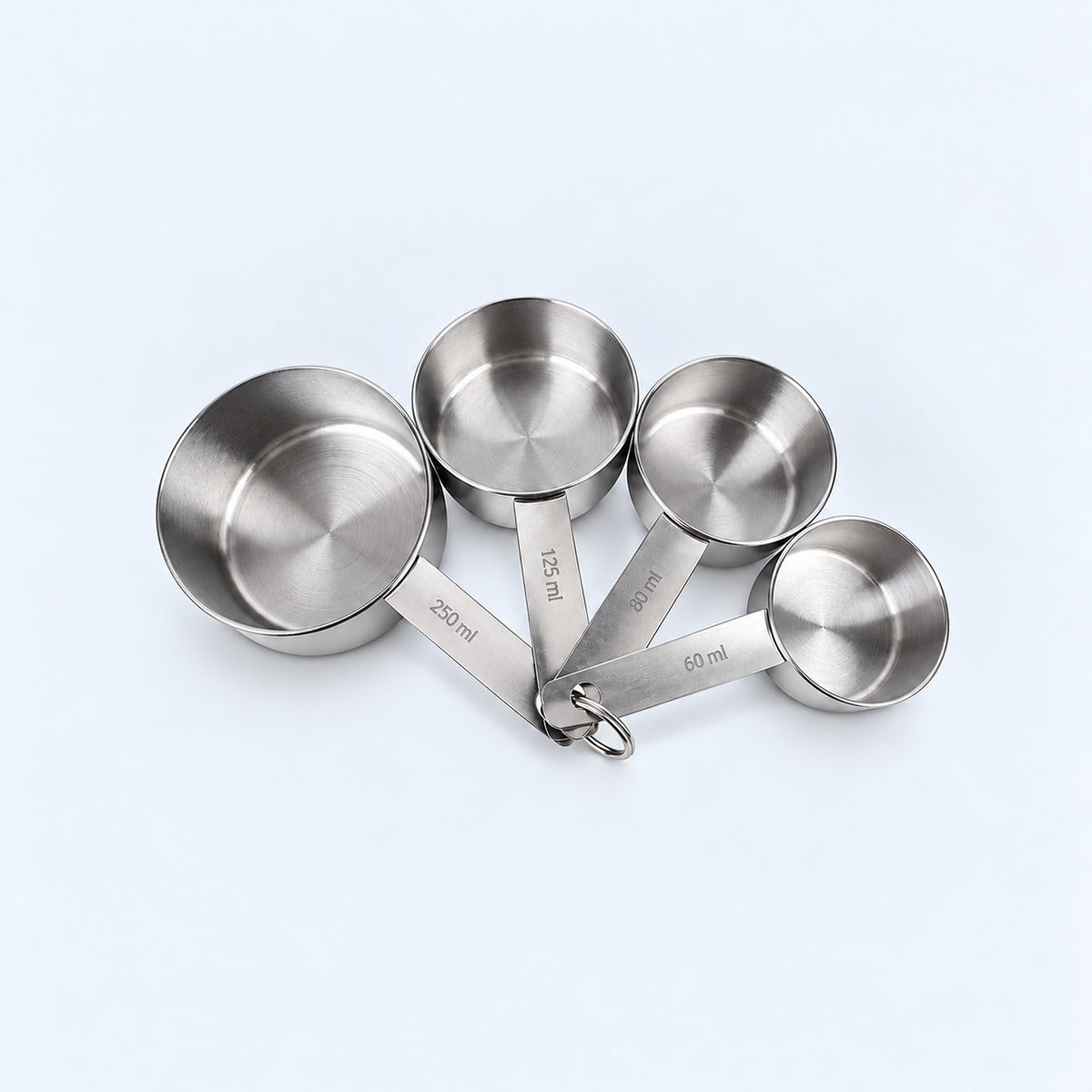 Four silver measuring cups on a pale gray studio background.