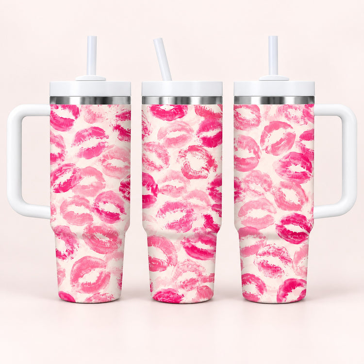 Three handled stainless steel tumblers with white lids and straws, decorated with a repeating pink lip print pattern on a light cream background, shown against a pale pink studio backdrop.