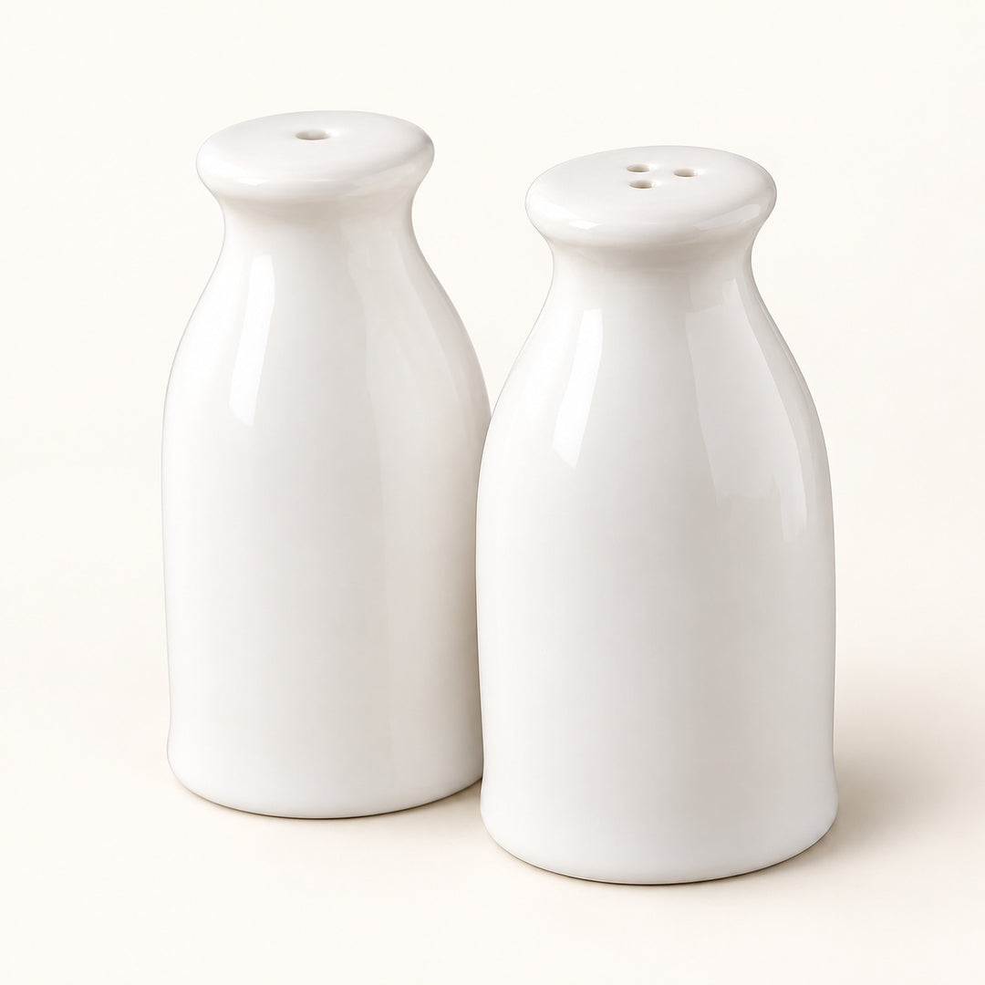 A pair of glossy white ceramic bottle-shaped salt and pepper shakers on a warm off-white background.