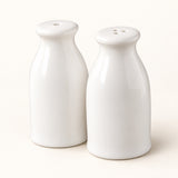 A pair of glossy white ceramic bottle-shaped salt and pepper shakers on a warm off-white background.