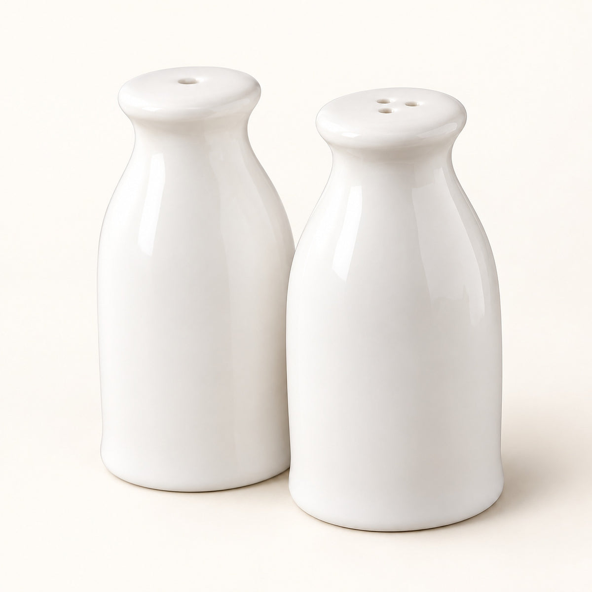 A pair of glossy white ceramic bottle-shaped salt and pepper shakers on a warm off-white background.