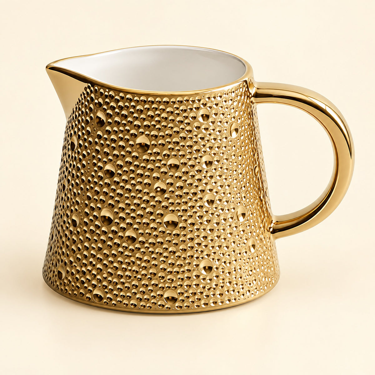A gold ceramic pitcher with a textured, dimpled exterior and a smooth white interior, shown on a light cream background.