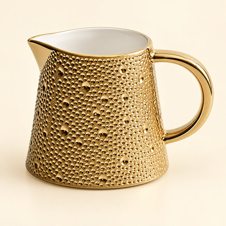 A gold ceramic pitcher with a textured, dimpled exterior and a smooth white interior, shown on a light cream background.