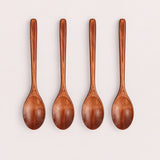 Four Brown wood spoons on a pale blush-gray studio background.