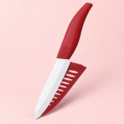 A kitchen knife with a matte red handle and matching red sheath, shown floating against a solid pale pink background.