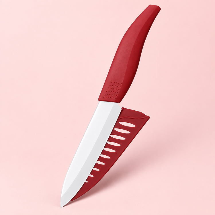 A kitchen knife with a matte red handle and matching red sheath, shown floating against a solid pale pink background.