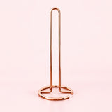 Empty rose-gold upright paper towel stand with open wire base.