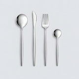 Silver four-piece flatware set on a pale gray studio background.