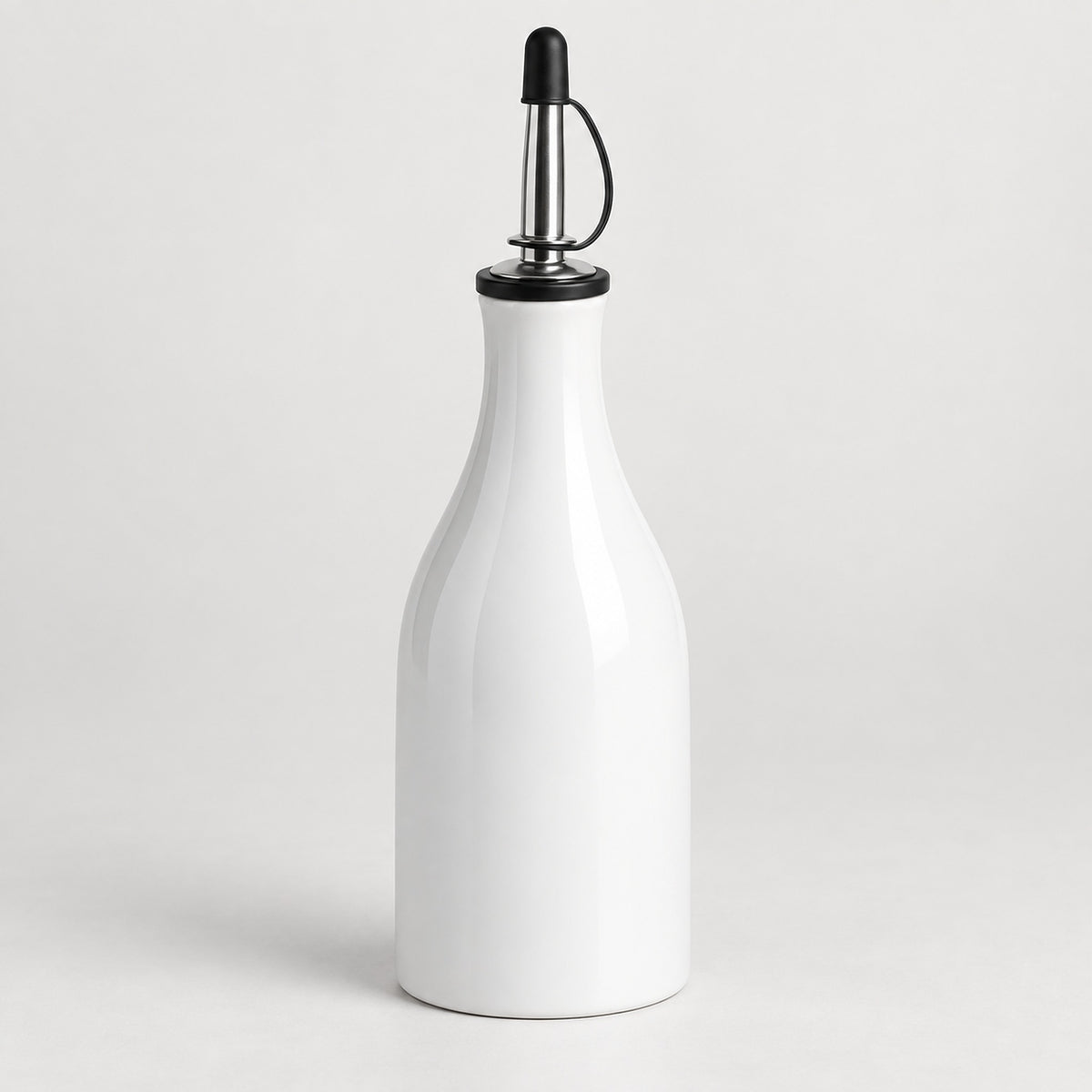 A white ceramic oil dispenser bottle with a polished stainless steel pour spout and a black plastic cap, set against a clean light gray background.