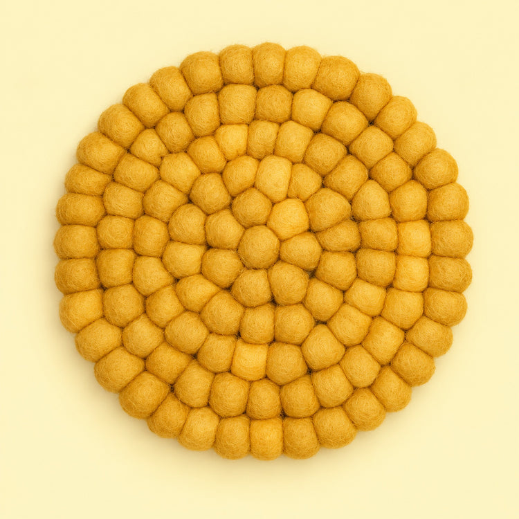 A round felt placemat or coaster made of small textured pom-pom balls, arranged in concentric circles, in a warm mustard yellow color on a light cream background.